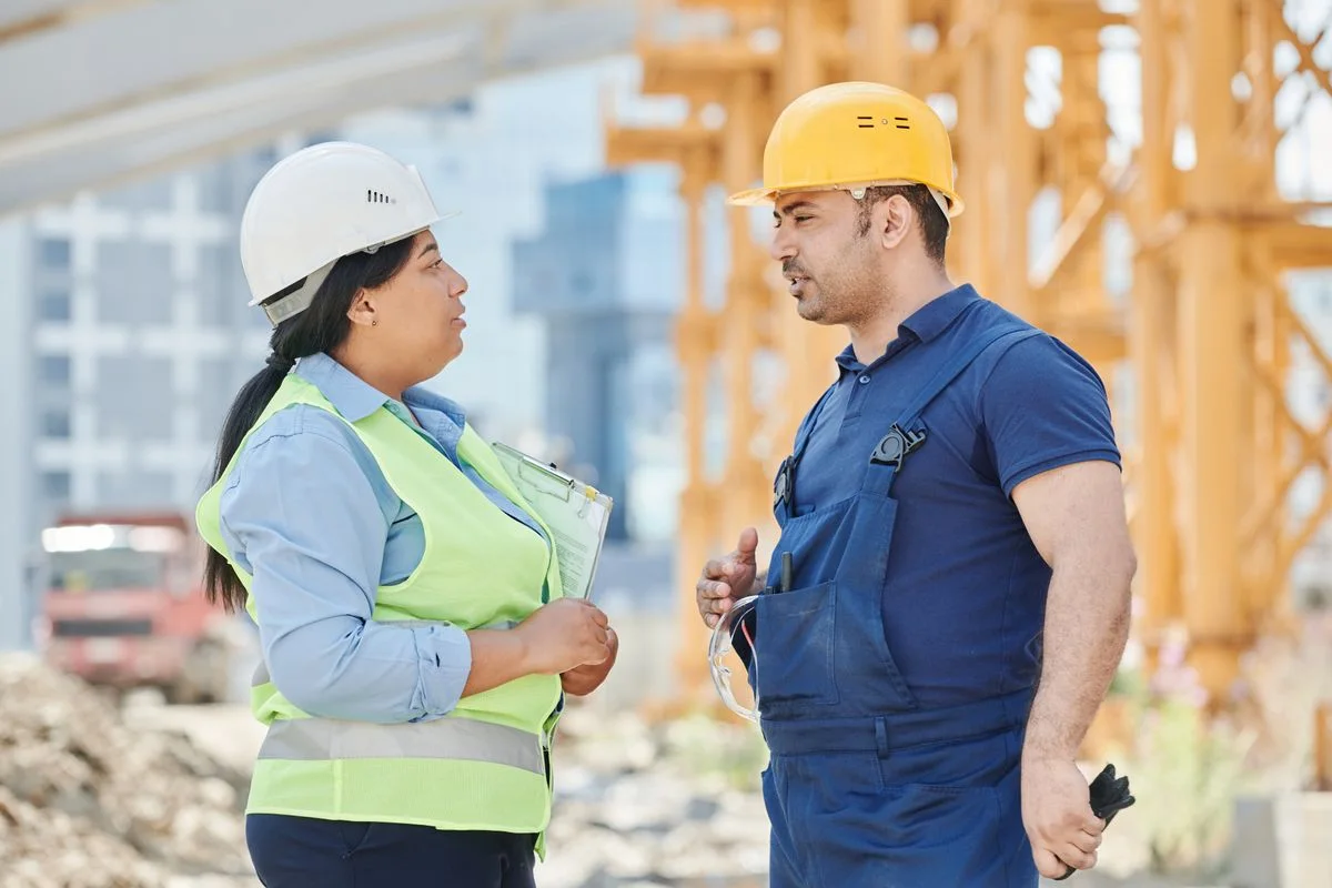 Two construction workers in hard hats discussing work at an active site